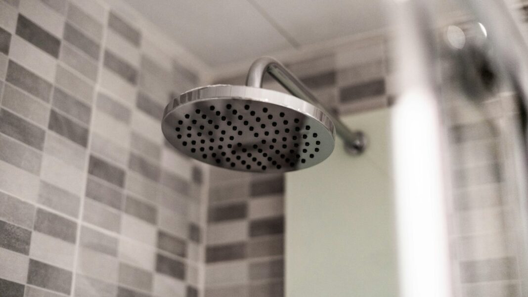 Warmwasser sparen, ohne bei der Hygiene zu sparen Duschkopf vor grau gefliester Wand