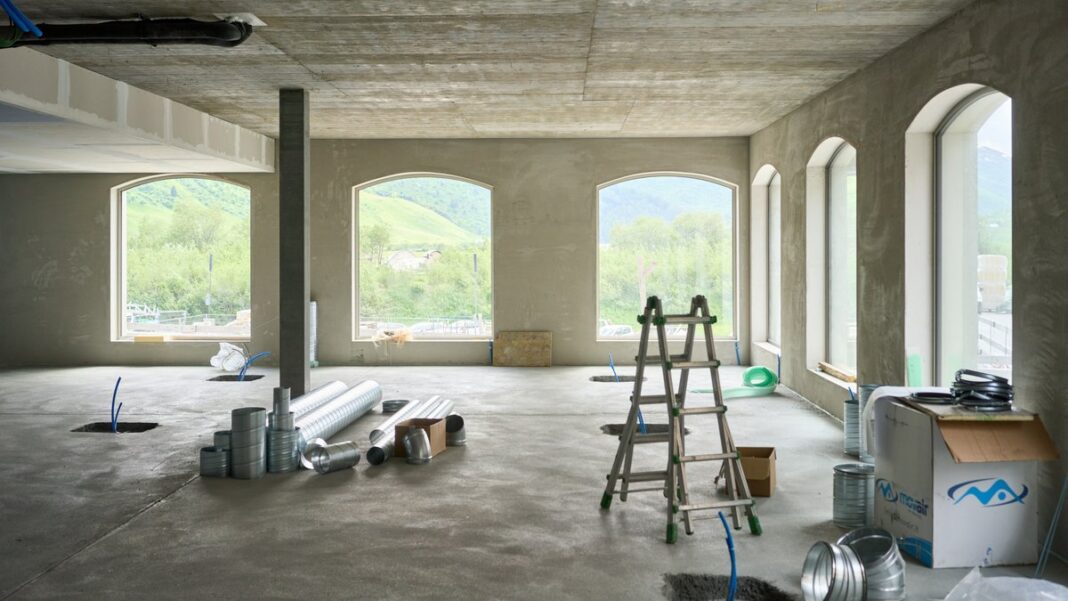 Rohbau-Innenraum mit Betonboden, Rundbogenfenstern und einer Leiter