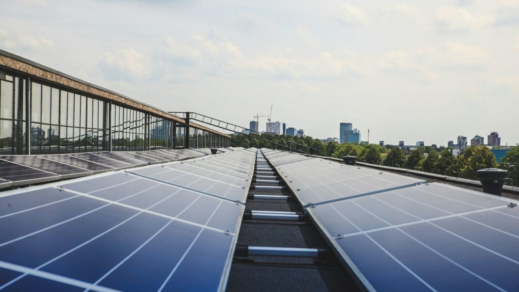 Reihen von Solarmodulen auf einem Flachdach, im Hintergrund eine Stadtsilhouette