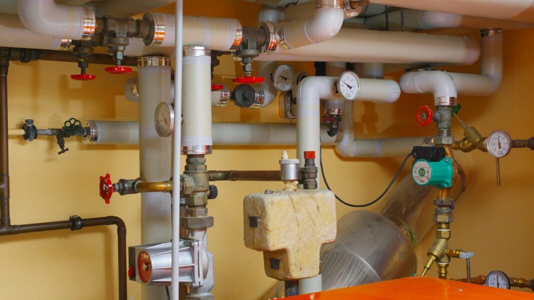 Heizraum mit Rohrleitungen, Ventilen, Umwälzpumpe und orangem Heizkessel