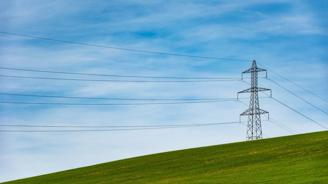 Hochspannungsmast mit Leitungen auf einer grünen Wiese unter blauem Himmel